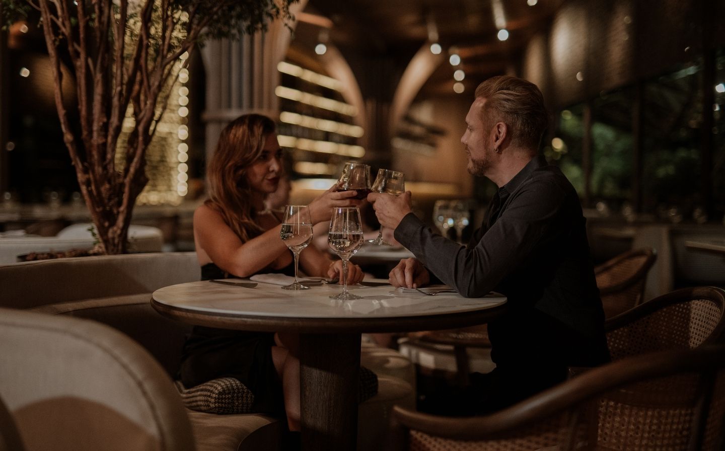 Dos personas levantando copas en un restaurante, disfrutando de una cena romántica.