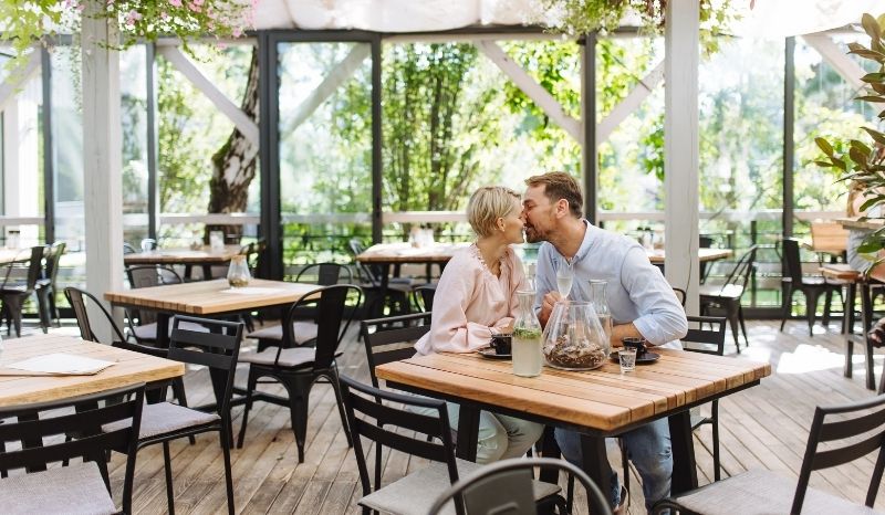 Pareja besándose en un restaurante, rodeados de una atmósfera romántica y luces suaves.