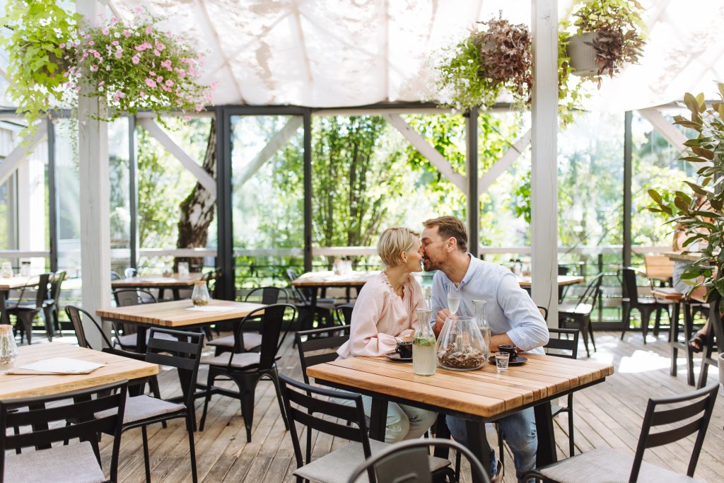Couple sharing a romantic kiss at a cozy restaurant table, surrounded by soft lighting and intimate decor.