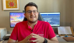 Hombre con camisa roja sentado en un escritorio frente a dos monitores encendidos.