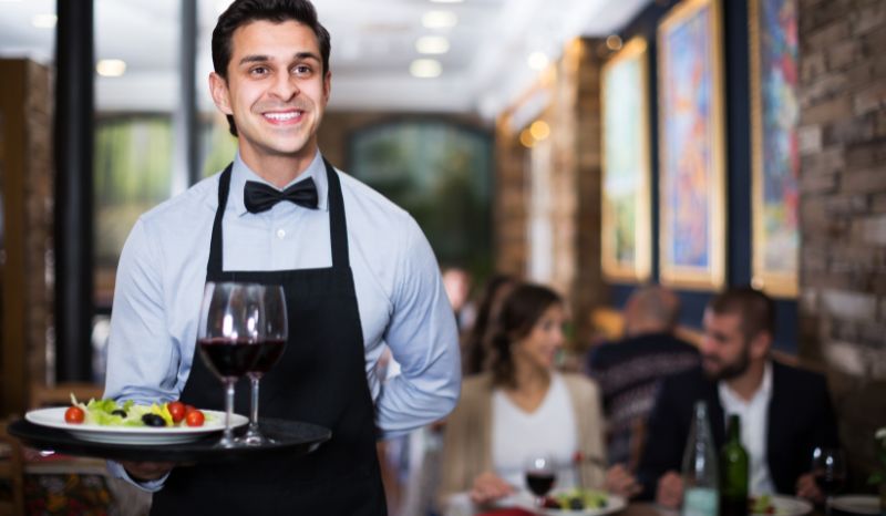 Mesero contento por su labor de entregar un plato a un cliente
