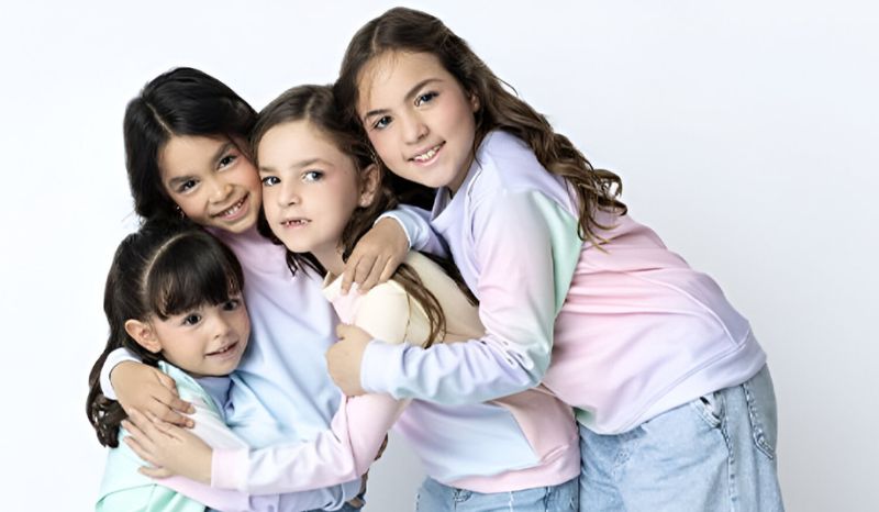 Tres niñas con suéteres a juego se abrazan, mostrando estilo y confianza en la moda deportiva de POPKIDS.