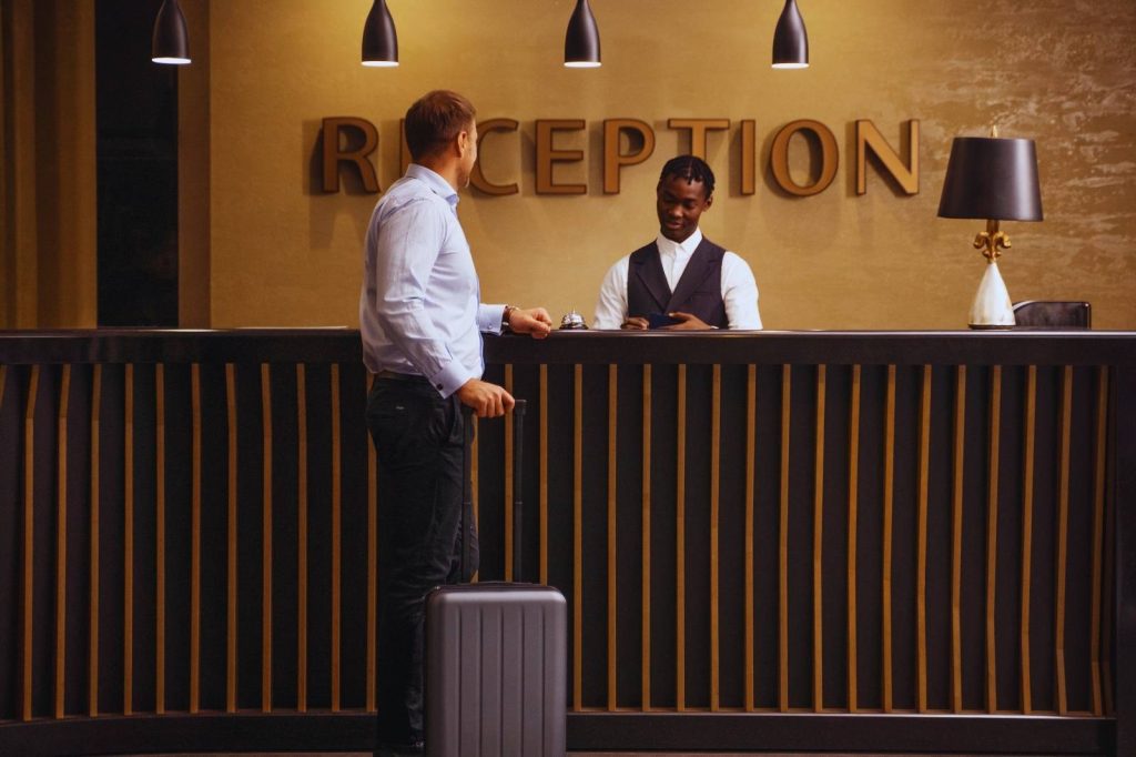 Man and receptionist standing next to the reception desk, conversing and smiling.