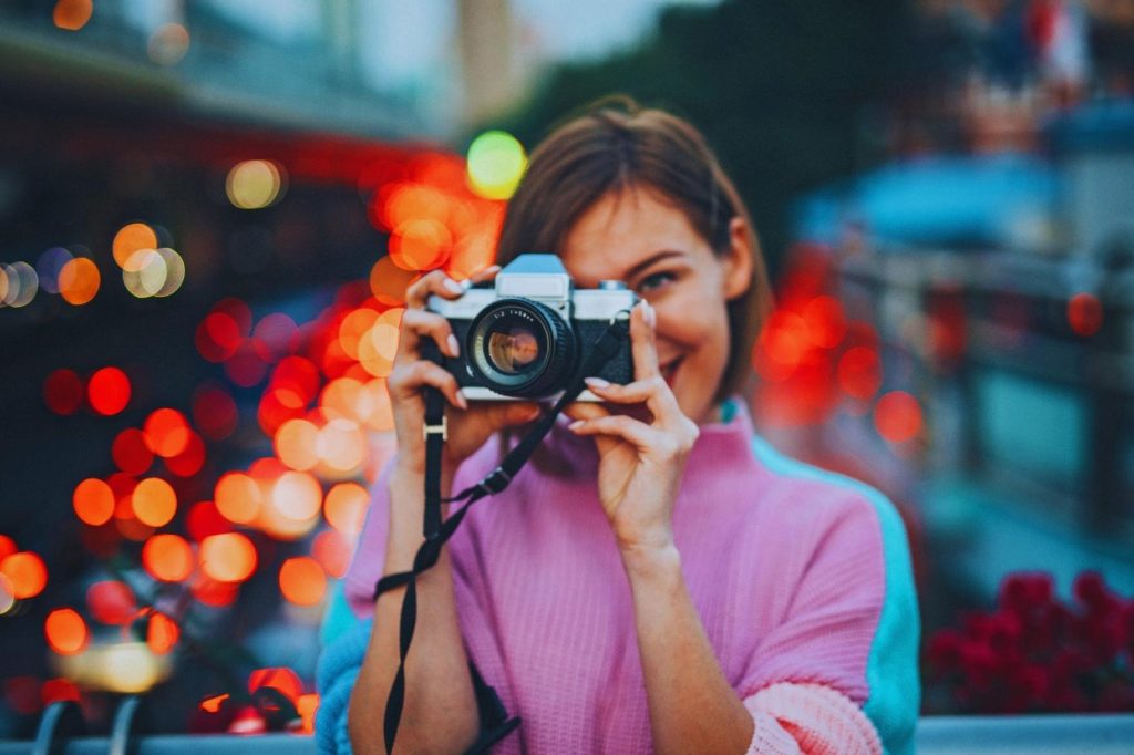 Mujer capturando una imagen con su cámara, sonriendo mientras fotografía.