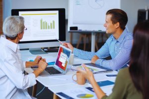 res personas sentadas a una mesa, mirando una pantalla de computadora.