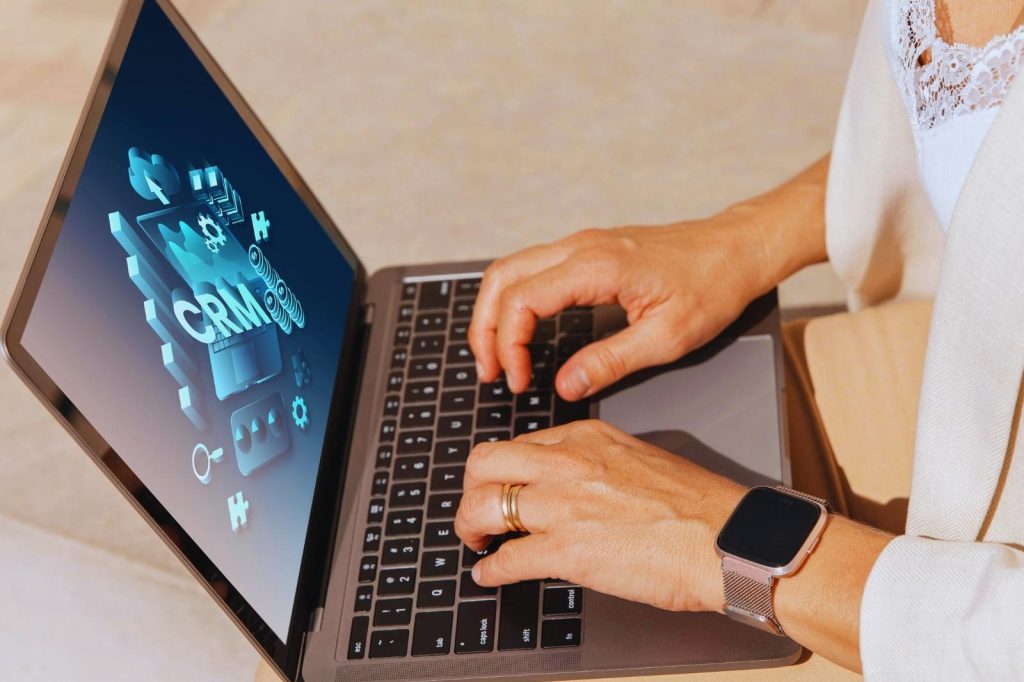 Mujer usando una laptop con la palabra "CRM" en la pantalla mientras escribe.