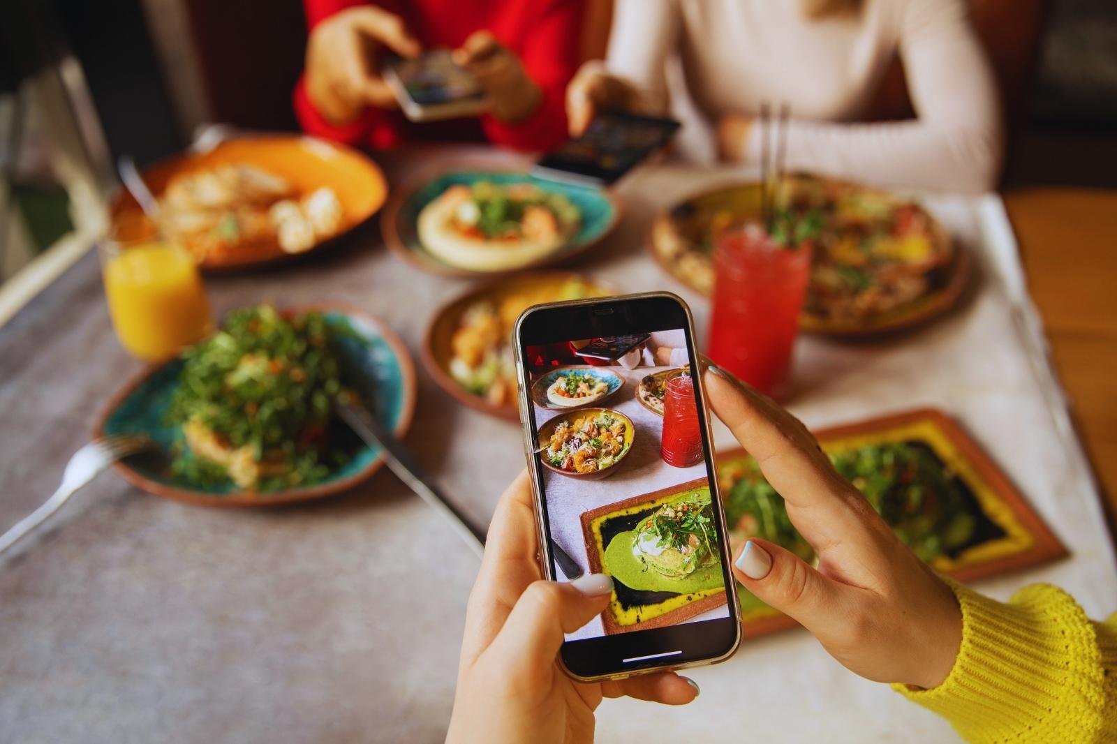 Una persona toma una foto de un plato de comida en una mesa, enfocándose en los detalles del platillo.
