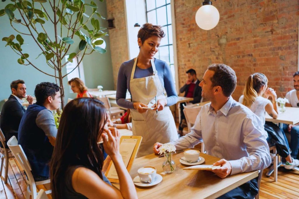 Una camarera sirviendo a los clientes en un restaurante, con una sonrisa mientras lleva platos a la mesa.