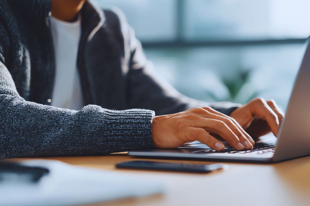 Persona tecleando en una computadora portátil en un entorno de trabajo.