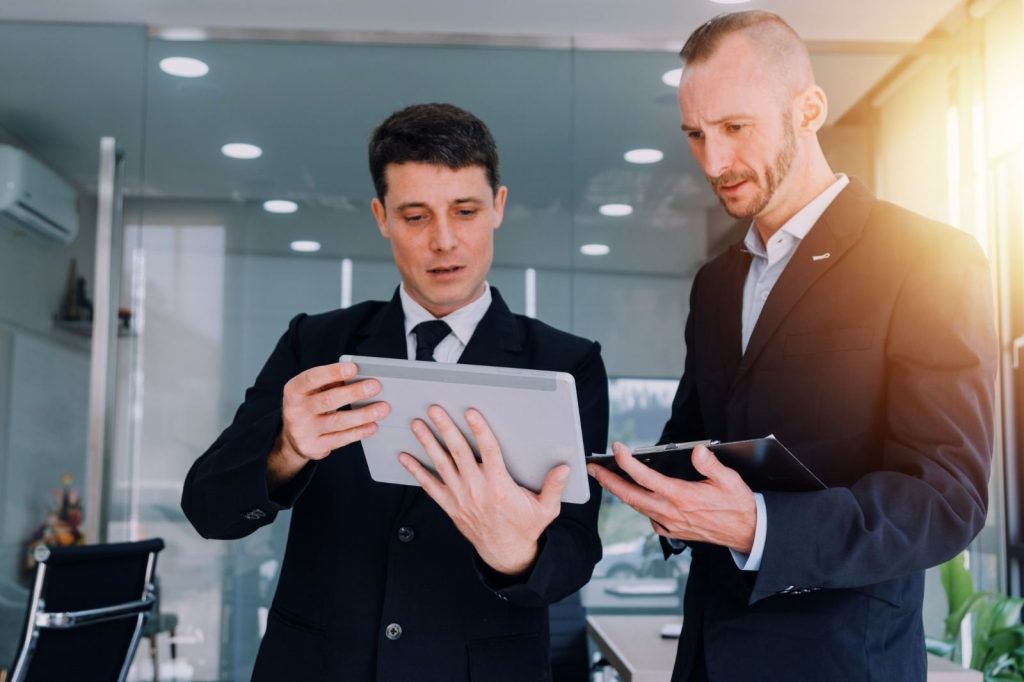 Dos hombres de negocios en traje revisan un tablet, discutiendo cómo leer un reporte digital.