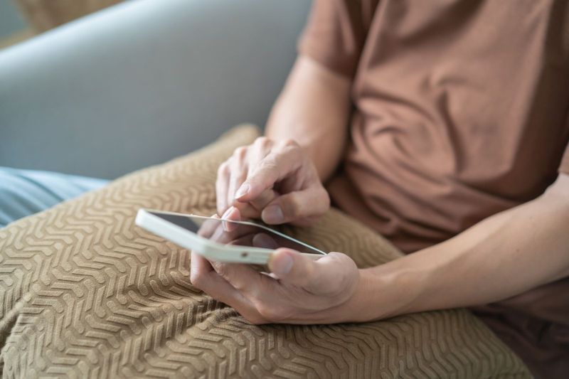 Hombre sentado en un sofá, sosteniendo un teléfono celular y mirando la pantalla con atención.
