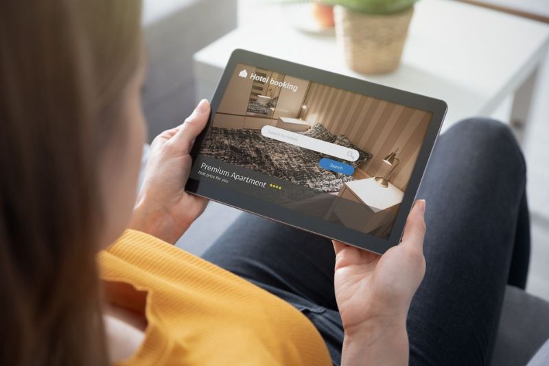 Mujer usando una tableta para buscar una habitación de hotel, con un mensaje de "De clic a silla ocupada" en pantalla.