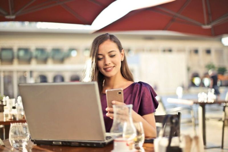 Mujer sentada en una mesa con un laptop y un teléfono celular, trabajando en un proyecto de landing page.
