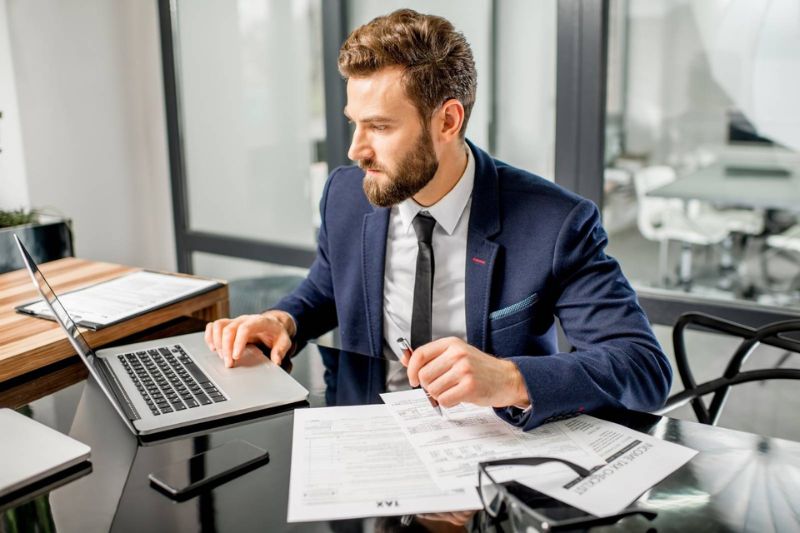 Hombre de traje sentado en un escritorio con un laptop, trabajando en una plantilla de landing.