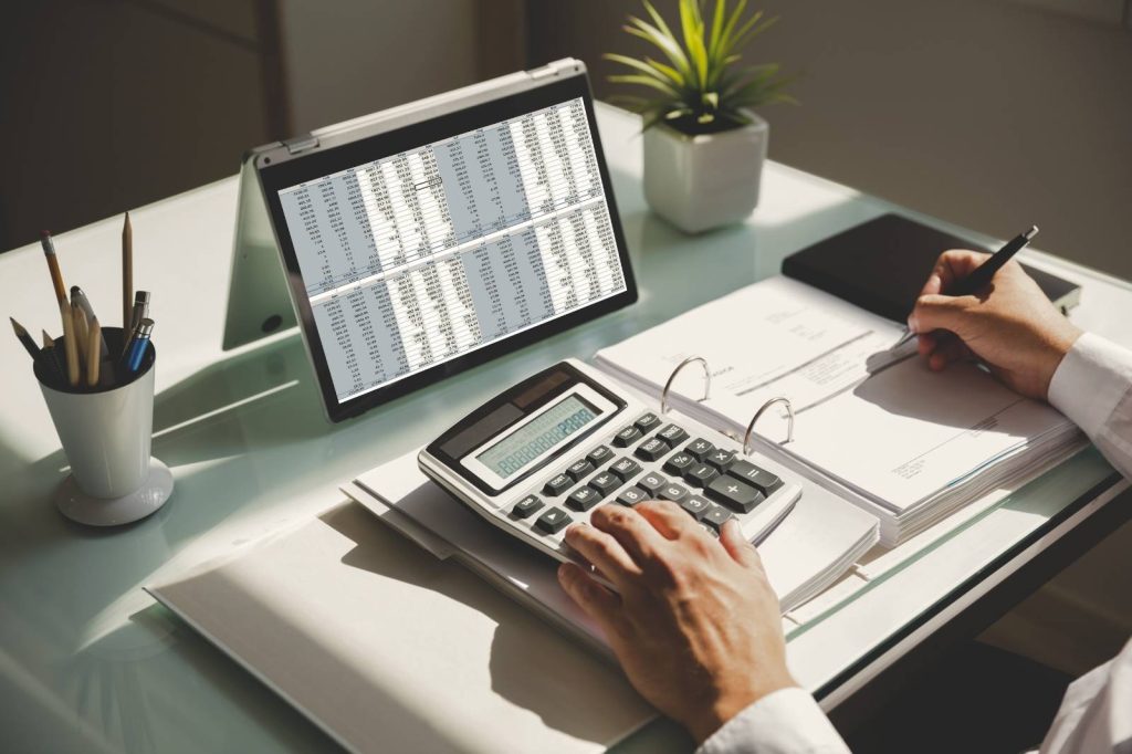 Hombre de negocios calculando datos financieros con una calculadora y un ordenador portátil.