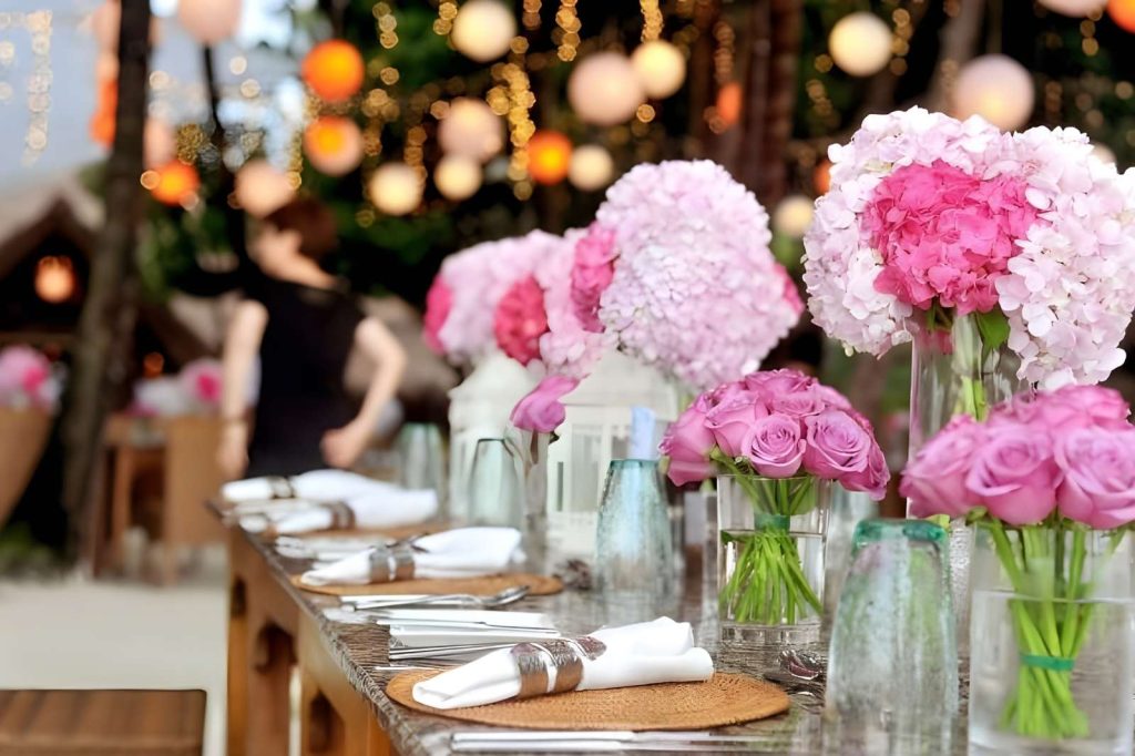 Mesa decorada con flores rosas y manteles blancos, lista para una comida elegante.