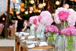 Mesa decorada con flores rosas y manteles blancos, lista para una comida elegante.
