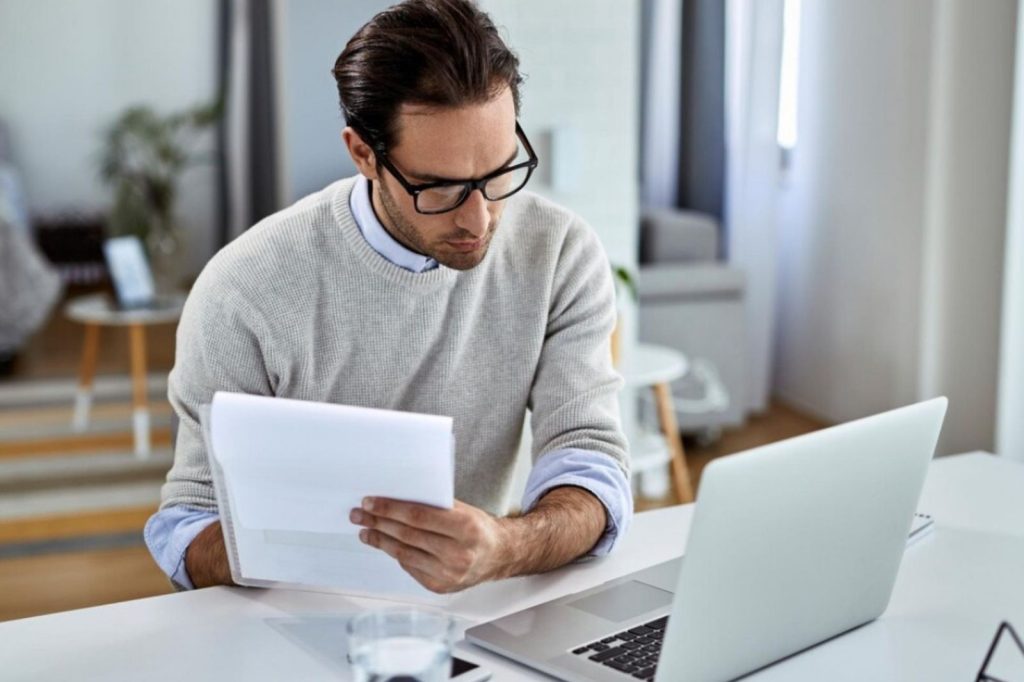Un hombre con gafas observa un documento en su laptop.