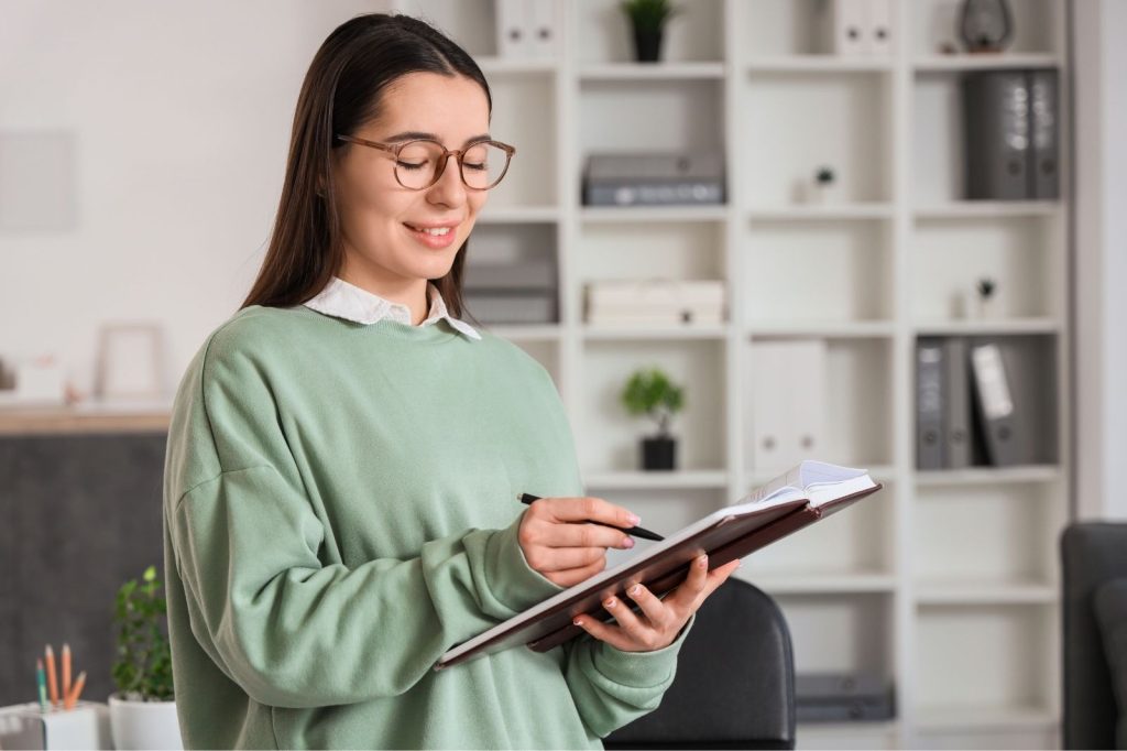 Mujer con gafas sostiene un clipboard y escribe en él.