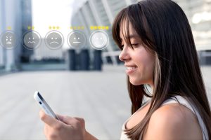 Mujer sonriente sosteniendo un teléfono inteligente con una carita feliz en la pantalla.