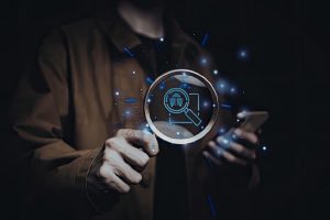Persona sosteniendo una lupa que resalta un icono de búsqueda digital brillante sobre un fondo oscuro.