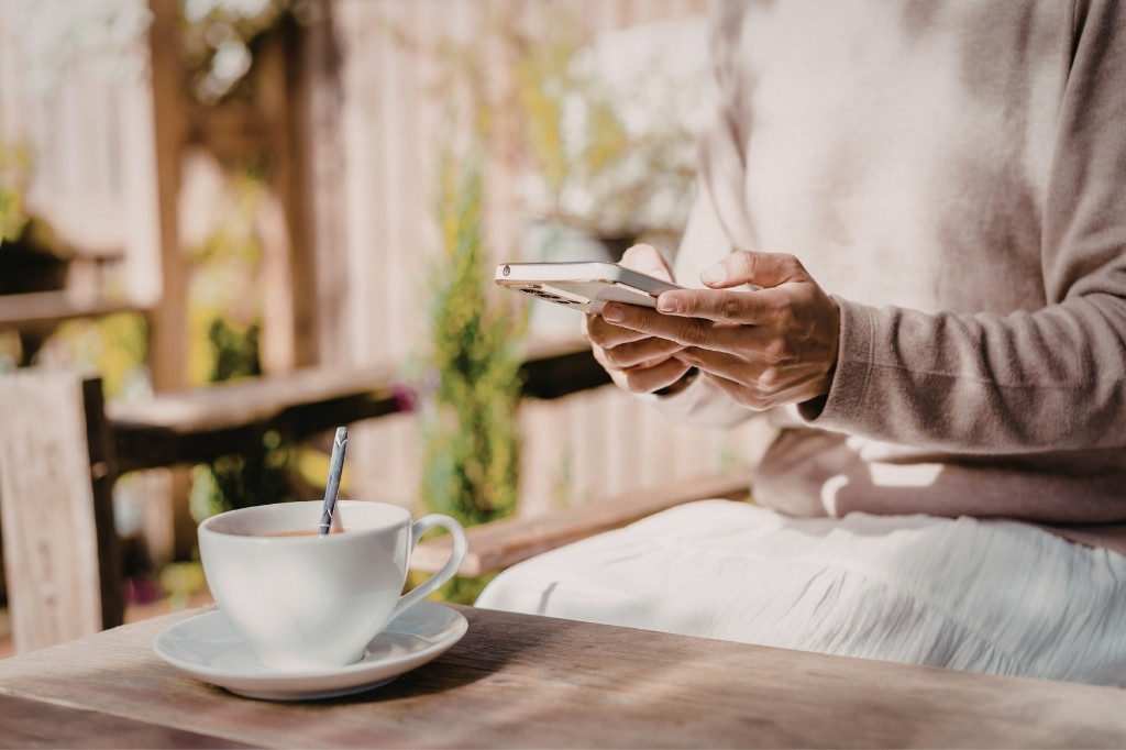 Cliente satisfecha usando su smartphone para realizar una recompra online mientras disfruta de un café en una terraza.