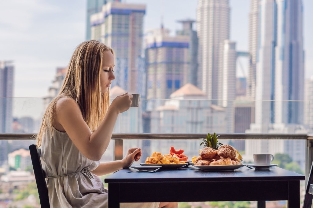 Huésped disfrutando de un desayuno gourmet en el balcón de un hotel boutique con vistas panorámicas a la ciudad.