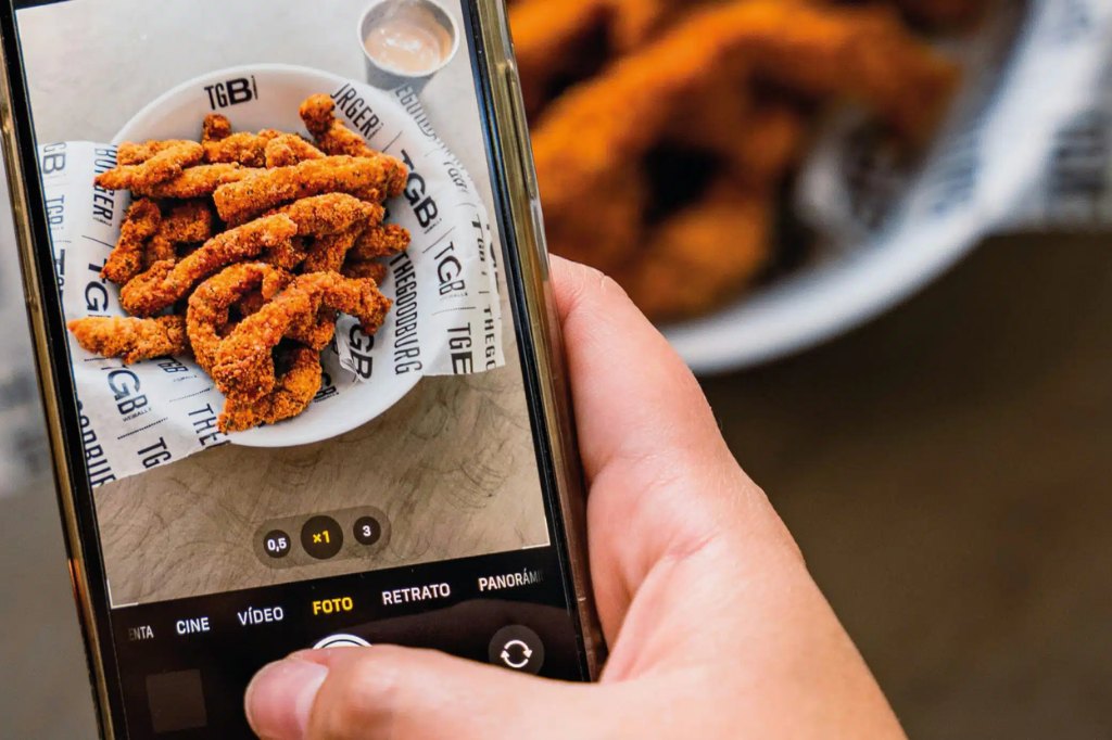 Persona tomando una foto con su smartphone a un plato de tiras de pollo crujientes
