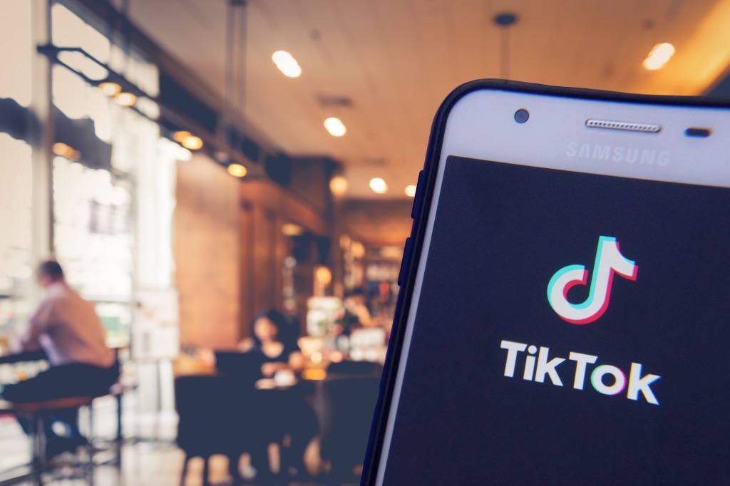Smartphone mostrando el logo de TikTok con el interior de un restaurante desenfocado al fondo.