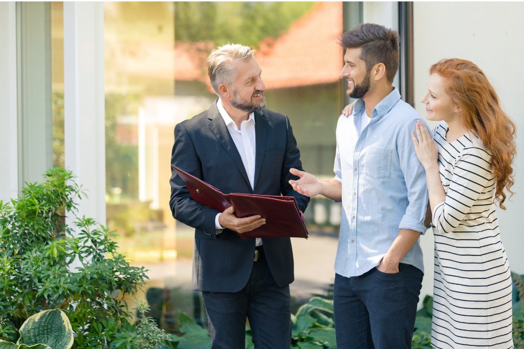Agente inmobiliario profesional asesorando a una pareja joven frente a una propiedad moderna en Medellín.