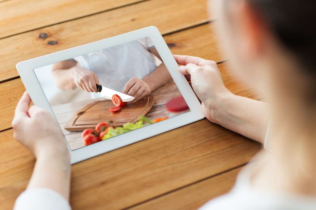 Persona viendo video de cocina en tablet con preparación de alimentos, reflejando contenido gastronómico que impulsa reservas.