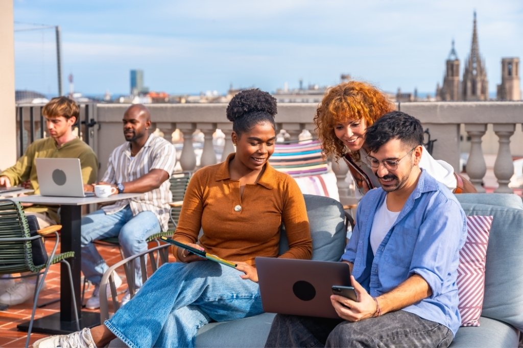 Nómadas digitales trabajando en rooftop con laptops y tablets, destacando espacios cómodos y conectividad en hotel de Medellín.