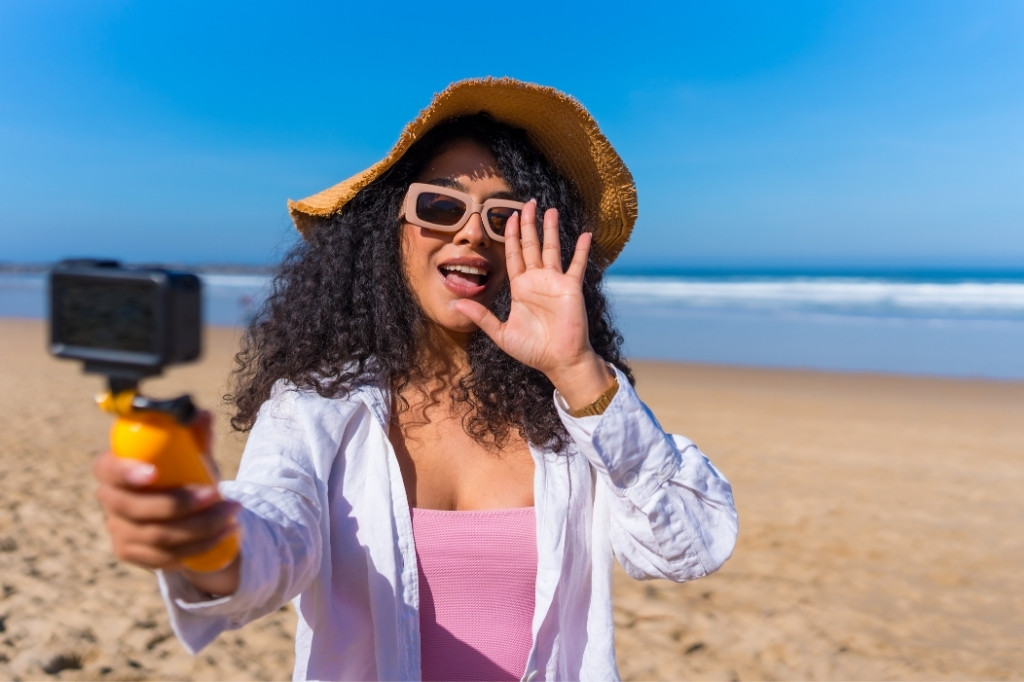 Creadora de contenido grabando video en la playa para TikTok, mostrando experiencia de viaje vinculada a reservas en hoteles boutique.